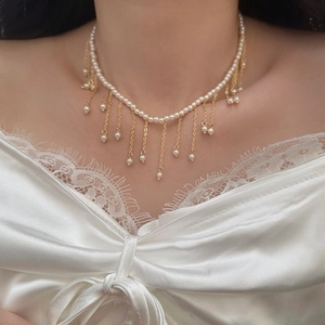 Close-up of elegant pearl fringe necklace with gold tassels on a white lace dress