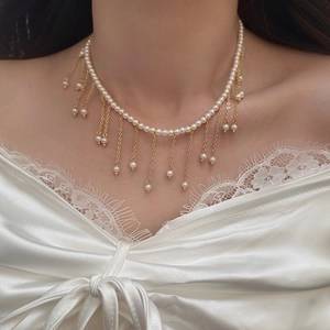 Close-up of pearl necklace with gold tassel fringes on model with white lace clothing