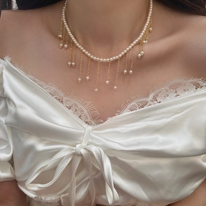 Detail of elegant pearl choker with gold chain tassels on lace fabric background