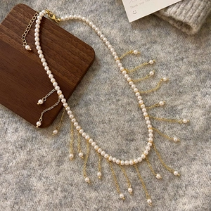 Detailed view of pearl tassel necklace with gold chains on soft grey knit background
