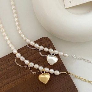 Détail du collier de perles baroques avec pendentifs cœur or et argent en design superposé