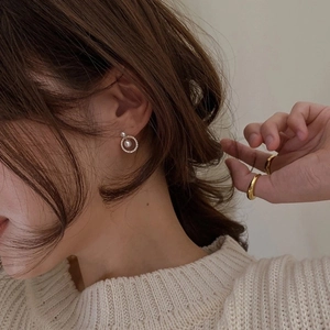 Close-up of geometric pearl earrings with zircons on a model wearing knitwear