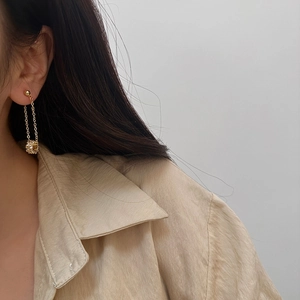 Close-up of golden tassel earrings with micro-pave zircon sphere worn by a model