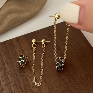 Detail of gold tassel earrings with black zircon pavé cylinders on a wooden display