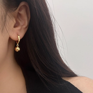 Elegant gold hoop earrings featuring polished spherical pendants worn by a female model