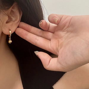 Detailed view of gold hoop earrings with polished sphere pendants on female model