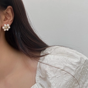 Close-up of a floral pearl stud earring with golden accents on a model's ear