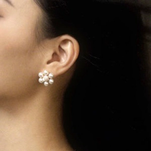 Detailed view of French-style pearl flower stud earrings worn on a model's ear