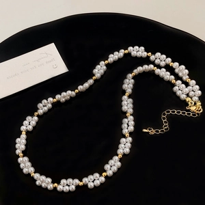 Gros plan d'un collier de perles avec grappes de fleurs et fermoir doré sur plateau noir