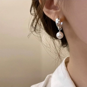Close-up of minimalist silver hoop earrings with white round pearl charm on model