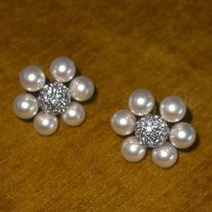 Detail of flower pearl stud earrings with pave diamond center on yellow velvet