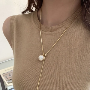Elegant gold snake chain with a large round white pearl pendant worn on a knit sweater