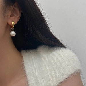 Detail shot of elegant geometric pearl earrings worn by a model in a minimal setting