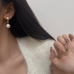 Close-up of elegant gold teardrop earrings with a hanging round white pearl on a model