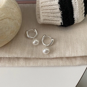 Detail of silver hoop earrings with round white pearls on minimalist fabric texture