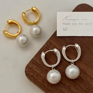 Minimalist gold and silver hoop earrings with large white pearls on a wooden tray