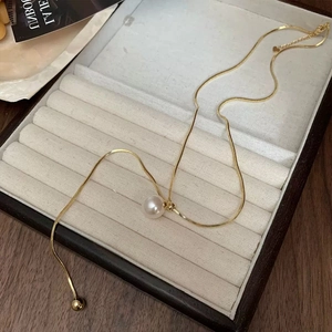 Detailed view of adjustable gold snake chain necklace with a single white pearl on velvet tray