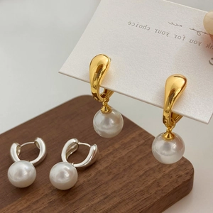 Detail of elegant gold and silver pearl drop earrings on a walnut wood base