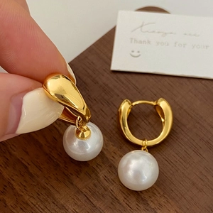 Close-up of elegant gold hoop earrings with white pearls shown on a wooden background