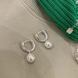 Macro detail of geometric S925 silver hoop earrings with white pearl pendants