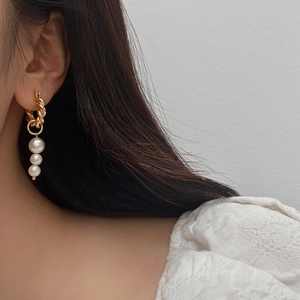 Close-up of gold twisted hoop earrings with triple white pearl drops on model