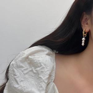 Elegant gold twisted hoop earrings featuring three vertical pearls on female model