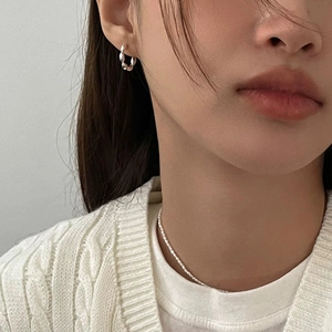 Elegant twisted silver hoops and delicate pearl necklace on a woman for a minimal look