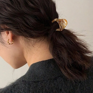 Detail view of model wearing tortoiseshell hair clip and twisted gold hoop earrings
