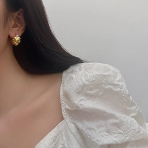 Close-up of elegant gold striped shell-shaped earrings worn by a model in soft light