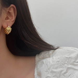 Detail shot of vintage golden shell-textured earrings with elegant pearl studs on ear