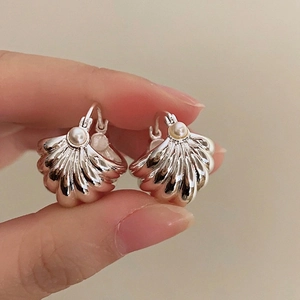 Macro view of shell-shaped silver earrings with glossy white pearl and ribbed texture
