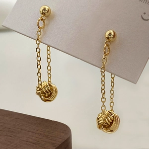 Detailed close-up of gold tassel earrings with spiral ball pendants on a white display card