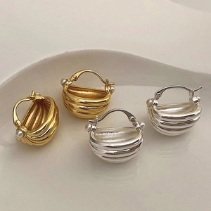 Detailed view of U-shaped gold and silver earrings with textured stripes and pearl accents