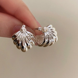 Detailed view of silver shell-shaped earrings with central pearl and ribbed texture