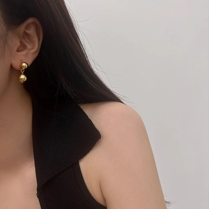 Close-up of minimalist double golden sphere drop earrings worn by a model on grey background