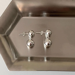 Detail of silver double ball drop earrings with polished finish on a steel tray