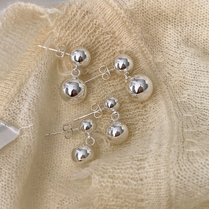 Detailed view of silver ball drop earrings on soft knit fabric showing mirror polish finish