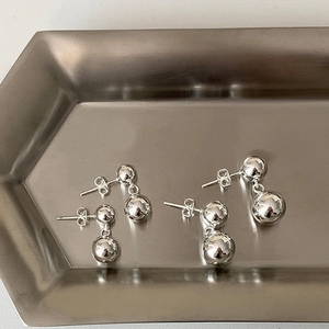 Detail of silver double ball drop earrings on a brushed metal tray showing polished finish