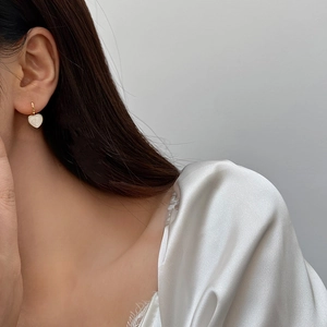Elegant gold-edged heart earrings with white shell inlay worn by a model in profile
