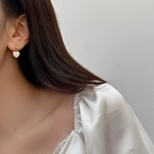 Detail of elegant heart-shaped earrings with gold hooks and white pearlescent pendants