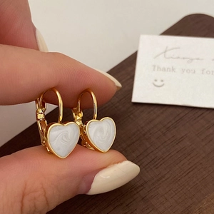 Detail view of heart-shaped gold leverback earrings with white marbled enamel texture