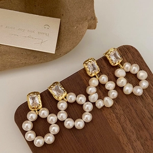 Elegant gold freshwater pearl drop earrings with zircon crystals on a wooden stand