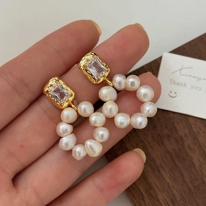 Macro shot of gold earrings with square zircon and irregular freshwater pearl circle