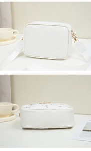 Detailed close-up of white crossbody bag featuring exquisite floral embroidery and golden zipper