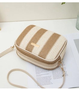 Close-up of woven straw camera bag featuring beige stripes and light gold metal hardware
