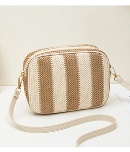 Detailed view of woven straw camera bag with vertical stripes and beige leather strap