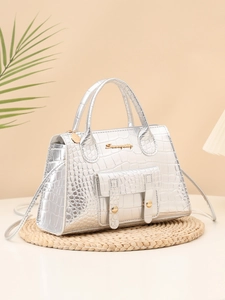 Macro view of silver crocodile pattern texture and metallic letter logo on stylish handbag