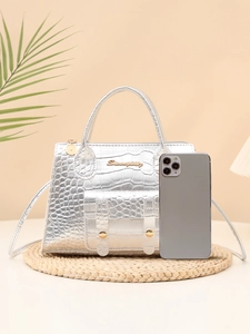 Detailed shot of silver crocodile pattern handbag with gold logo and shoulder strap