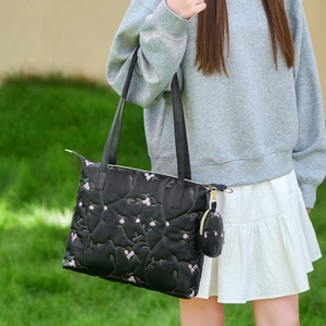 Black quilted tote bag with floral embroidery and mini pouch carried by a model outdoors