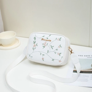 White crossbody camera bag with pink floral embroidery and adjustable strap